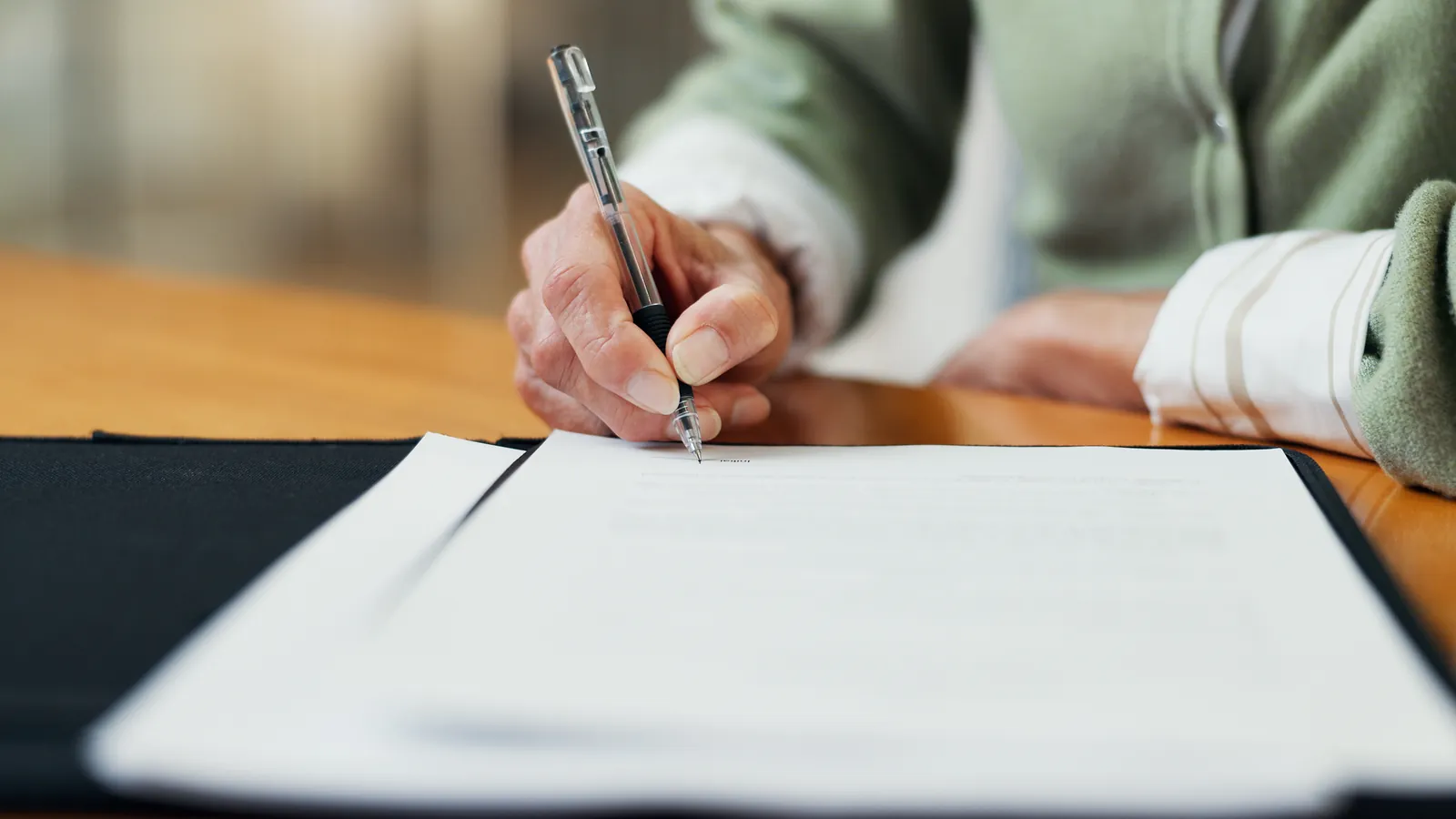 Hands holding a pen over paperwork on a desk.